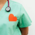 Nurse in pastel green scrubs with stethoscope and paper heart for heart health awareness.